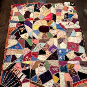 May include: A vintage patchwork quilt with a variety of fabrics and colors, including velvet, silk, and satin. The quilt is hand-stitched and features intricate embroidery details. The quilt is a beautiful example of traditional American quilting.