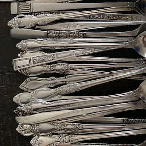 Puede incluir: Una colección de cucharas de plata vintage con mangos ornamentados. Las cucharas están dispuestas en una fila, con los mangos mirando al espectador. Las cucharas tienen todos diseños diferentes, pero todas tienen un estilo similar.