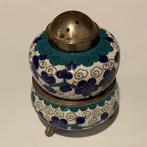 Könnte beinhalten: Ein weißer, blauer und grüner Cloisonné-Salzstreuer mit silbernem Deckel und drei Beinen. Der Salzstreuer ist mit einem Blumenmuster verziert.