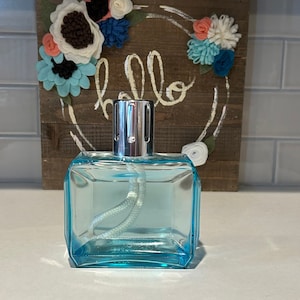 May include: A clear glass oil lamp with a blue tint and a white wick. The lamp is sitting on a white surface.