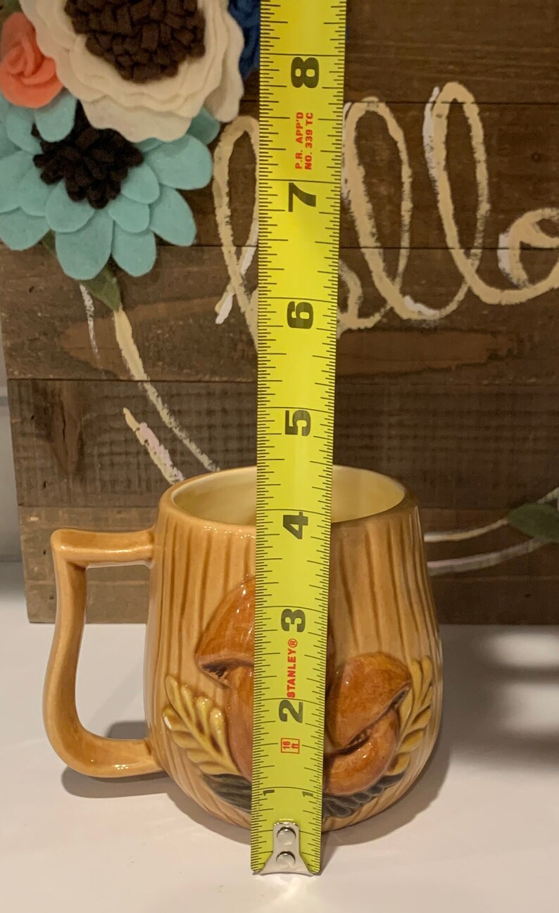 May include: A brown ceramic mug with a mushroom design. The mug is 4 inches tall and has a handle.