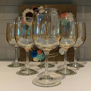 May include: Set of six clear glass wine glasses with a gold iridescent finish. The glasses are arranged in a circle on a white surface.