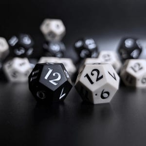 May include: A selection of black and white twelve-sided dice, with the number 12 visible on the faces of two dice in the foreground. The dice are set against a dark background, creating a contrast.