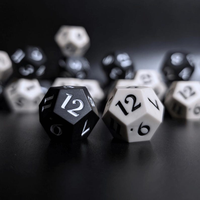 May include: A selection of black and white twelve-sided dice, with the number 12 visible on the faces of two dice in the foreground. The dice are set against a dark background, creating a contrast.