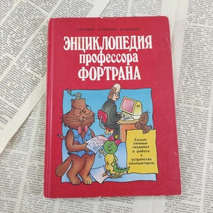 Op de afbeelding: Een rood boek met de titel "Enciclopedia Profesora Fortran" en illustraties van een kat, een insect en een persoon die een computer gebruikt. Het boek gaat over computerprogrammeren.