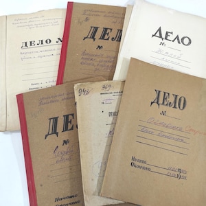 May include: A collection of six vintage paper file folders in shades of tan and cream. Each folder features the Cyrillic text "ДЕЛО" printed in black, with handwritten notes, lines for dates, and red binding tape on some edges.