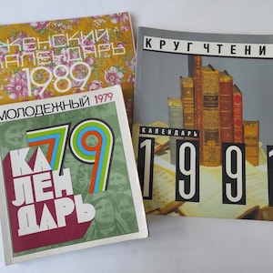 Puede incluir: Tres calendarios vintage de 1979, 1989 y 1991. El calendario de 1979 es un calendario juvenil con un diseño rojo, blanco y azul. El calendario de 1989 es un calendario femenino con un diseño floral. El calendario de 1991 es un calendario de lectura con una portada gris y una pila de libros.