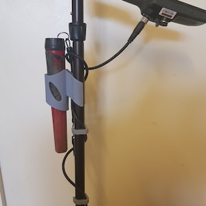 Puede incluir: Un detector de metales negro con una bobina gris y roja unida al lateral. El detector tiene un mango negro y un panel de control negro con una pantalla. El detector está montado en un poste negro con bridas de cable grises.