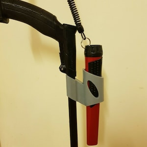 Könnte beinhalten: Ein roter Metalldetektor mit einem grauen 3D-gedruckten Halter, der an der Stange befestigt ist. Eine schwarze Taschenlampe ist im Halter befestigt.