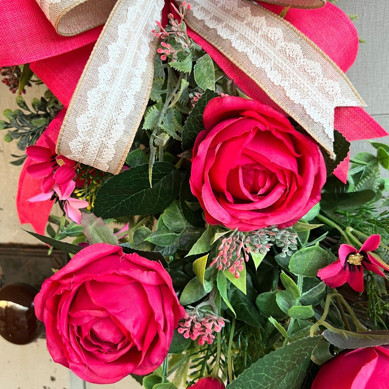 The hot pink cabbage roses are accented with pink wildflowers and beautiful greenery. The design cascades down the left side of the grapevine. The pink and burlap and white striped bow makes this everyday design look exquisite for any occasion.