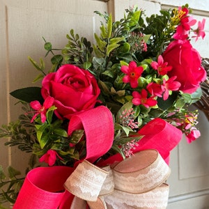 The hot pink cabbage roses are accented with pink wildflowers and beautiful greenery. The design cascades down the left side of the grapevine. The pink and burlap and white striped bow makes this everyday design look exquisite for any occasion.