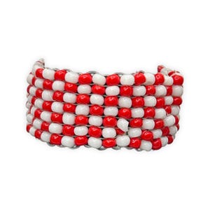 K&ouml;nnte beinhalten: Ein breites Armband aus abwechselnd roten und wei&szlig;en Perlen. Die Perlen sind mit einer silberfarbenen Schnur aufgef&auml;delt, wodurch ein gewebtes Muster entsteht. Das Armband ist gebogen und scheint aus Kunststoffperlen zu bestehen.