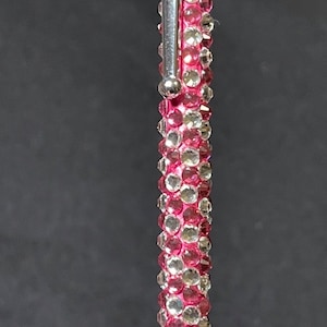 May include: A pink pen covered in clear and pink rhinestones.