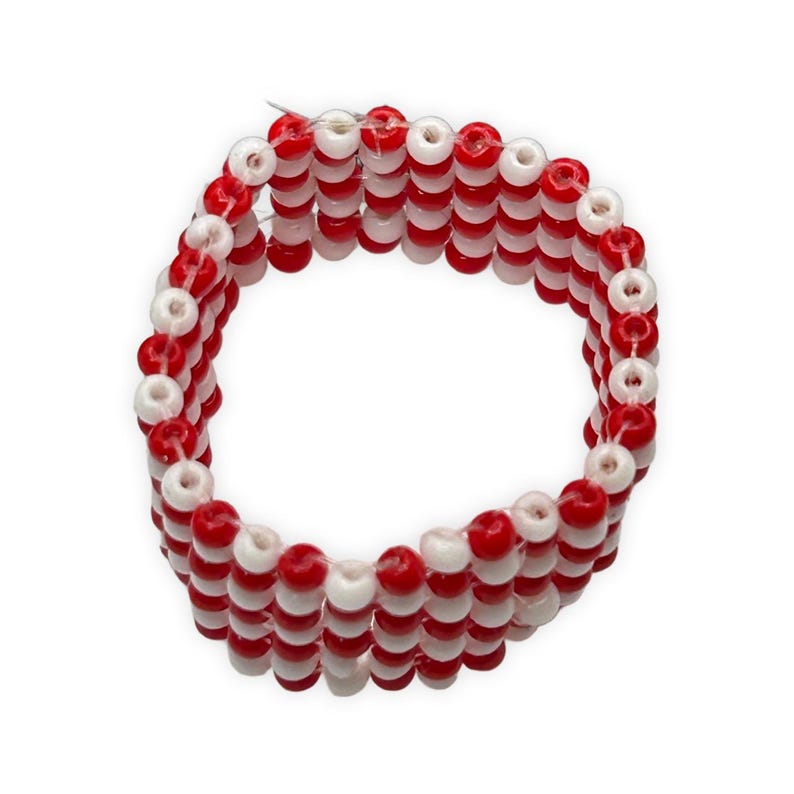 K&ouml;nnte beinhalten: Ein Armband aus abwechselnd roten und wei&szlig;en Perlen. Das Armband besteht aus mehreren Str&auml;ngen von Perlen, wodurch ein geschichteter Effekt entsteht. Die Perlen sind klein und rund, und das Gesamtdesign ist schlicht und farbenfroh.