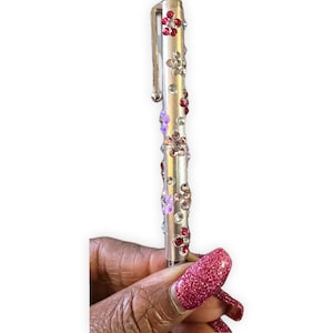 Puede incluir: Un bolígrafo plateado con un diseño de flores transparentes y rosas. El bolígrafo está decorado con diamantes de imitación.