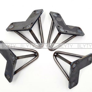 May include: Four metal triangle-shaped furniture legs with a flat base. The legs are made of a dark metal and have a slightly distressed finish.
