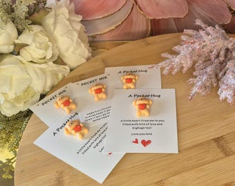 May include: Four small cards with a pocket hug theme. Each card has a small, brown, clay figurine of a dog holding a red heart. The cards have text that reads "A Pocket Hug" and "Here's a little hug. Please keep it safe, then it will be with you when you need it."  "A little heart from me to you, filled with lots of love and bighugs too! Love you lots."