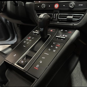 May include: Close-up of a black car interior with a gear shifter, buttons, and a digital display. The display shows "8.10" and "AUTO".
