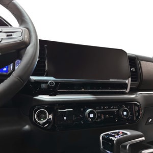 May include: A black leather-wrapped steering wheel with a silver control panel. The dashboard features a large black touchscreen display and a row of silver buttons.