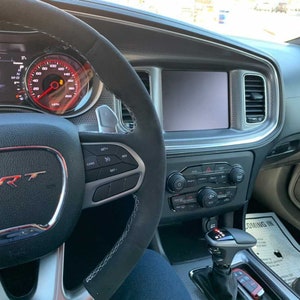 May include: The interior of a black Dodge Charger SRT with a black leather steering wheel, a digital instrument cluster, and a touchscreen infotainment system. The car has a black leather interior with red stitching.