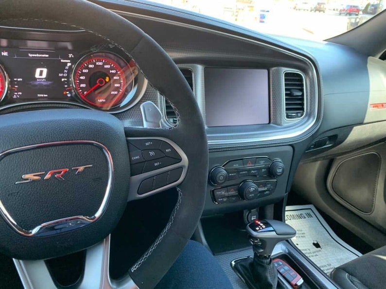 May include: The interior of a black Dodge Charger SRT with a black leather steering wheel, a digital instrument cluster, and a touchscreen infotainment system. The car has a black leather interior with red stitching.