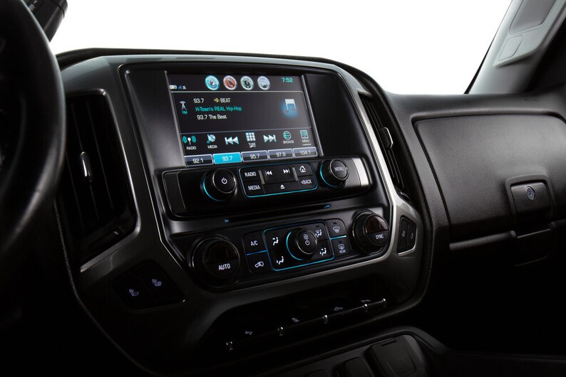 May include: A black car dashboard with a touchscreen display showing a radio station playing music. The display also shows the time, temperature, and other information. The dashboard has several buttons and knobs for controlling the radio, climate control, and other vehicle functions.