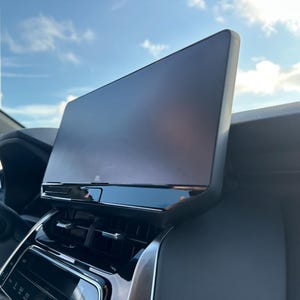 May include: A black car interior with a large, horizontal touchscreen display. The screen is positioned above the dashboard and is angled slightly towards the driver.