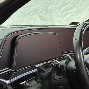 May include: Close-up of a black leather-wrapped steering wheel and a black dashboard with a large touchscreen display in a car interior.