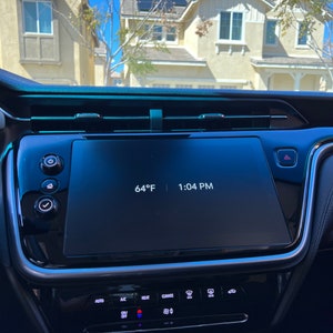 May include: A car's dashboard with a digital display showing the temperature as 64°F and the time as 1:04 PM. The display is surrounded by black plastic and has several buttons below it.