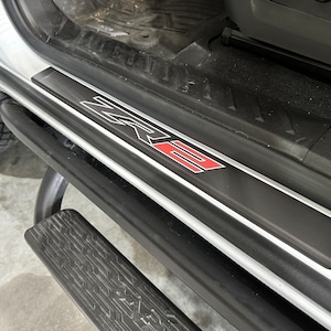 May include: Close-up of a black and silver car door sill with the word "Z71" in red lettering.