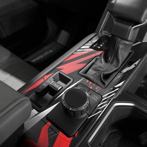 May include: Close-up of a black car interior with a red and white graphic design. The image shows a gear shifter, a 4WD selector, and a knob labeled "Tow Haul".