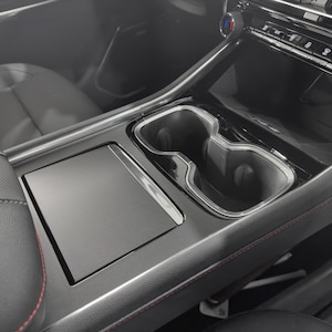 May include: A black car interior with a center console featuring a storage compartment, two cup holders, and a black leather armrest.