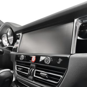 May include: A black car interior with a large touchscreen display, two round buttons, and a silver air vent.