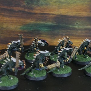 May include: A group of ten green and gold painted miniature lizard warriors with swords and shields. The miniatures are posed in a battle formation on a green base.