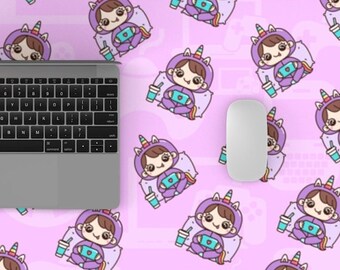 Puede incluir: Una alfombrilla de escritorio rosa y blanca con un patrón repetido de unicornios de dibujos animados que llevan pijamas y sostienen una taza de café. Un ordenador portátil y un ratón inalámbrico están sobre la alfombrilla de escritorio.