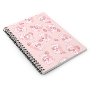 May include: A pink spiral notebook with a repeating pattern of strawberry milk cartons and strawberries. The cartons are white with pink lids and say "Strawberry Milk" on them.
