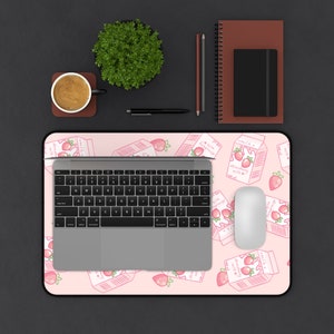 Peut inclure: Un tapis de souris rose et blanc avec un motif r&eacute;p&eacute;t&eacute; de cartons de lait &agrave; la fraise. Un ordinateur portable, une souris et une tasse de caf&eacute; sont sur le tapis de souris.