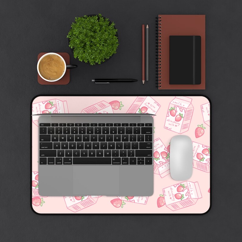 Peut inclure: Un tapis de souris rose et blanc avec un motif r&eacute;p&eacute;t&eacute; de cartons de lait &agrave; la fraise. Un ordinateur portable, une souris et une tasse de caf&eacute; sont sur le tapis de souris.