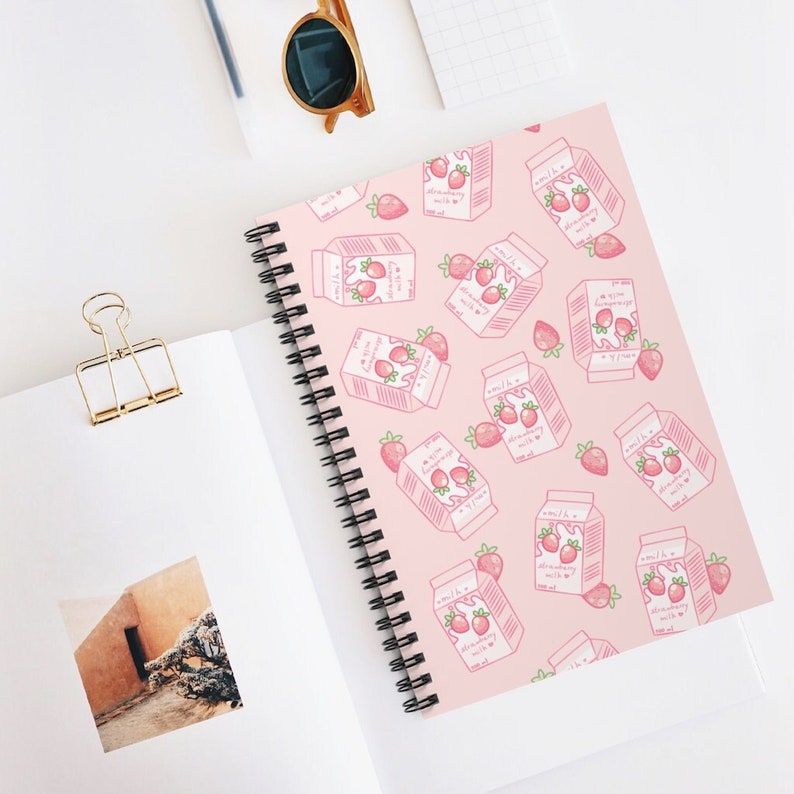 May include: A pink spiral notebook with a repeating pattern of pink milk cartons with strawberries and the text "milk & strawberry" on them.