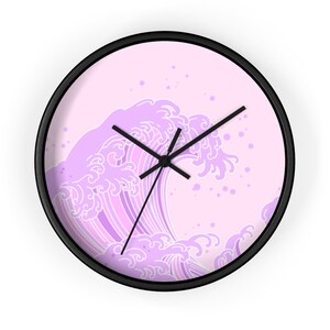 May include: A pink and white wall clock with a black frame features a stylized image of a large wave in a Japanese style. The wave is outlined in white and filled with shades of purple.