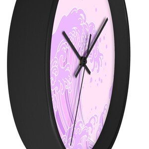 May include: A black framed clock with a pink and white wave design. The wave is stylized and has a Japanese aesthetic.
