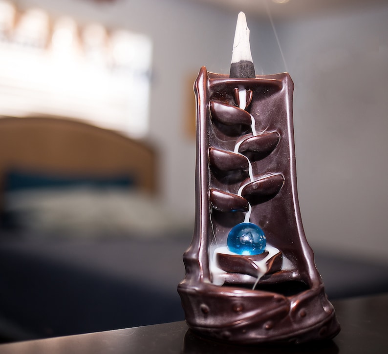 May include: A brown ceramic incense burner with a blue glass ball in the center. Smoke flows from the top of the burner, creating a waterfall effect.