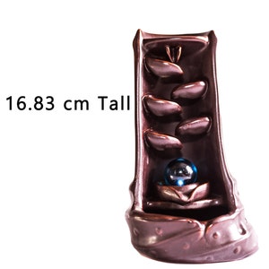 May include: A brown ceramic incense burner shaped like a waterfall with a blue glass ball at the bottom. The burner is 16.83 inches tall.