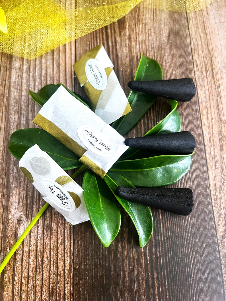 May include: Three black incense cones on a green leaf with three small packages of incense. The packages are labeled "Ocean Mist", "Cherry Vanilla", and "Dolce Melya".