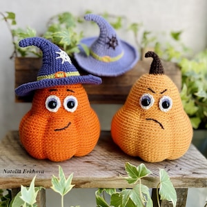 Op de afbeelding: Handgemaakte gehaakte pompoenen met grappige gezichten en heksenhoeden. Eén pompoen draagt een blauwe hoed met een witte ster, een andere heeft een boze uitdrukking. De pompoenen zijn oranje en bruin, perfect voor Halloween.