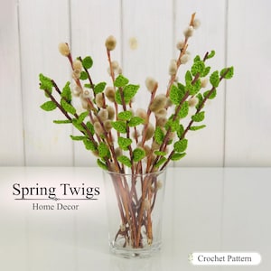 Op de afbeelding: Een doorzichtige glazen vaas met een boeket bruine takjes met pluizige beige katjes en kleine, felgroene gehaakte blaadjes. De tekst Spring Twigs Home Decor en Crochet Pattern is zichtbaar op de afbeelding tegen een witte achtergrond.