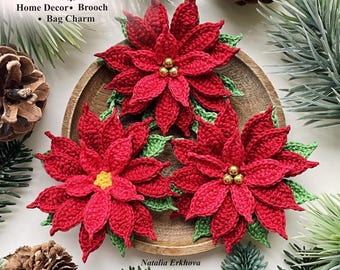 May include: Three crocheted poinsettia flowers with vibrant red petals and green leaves. Two flowers feature small gold beads at the center, while one has a yellow center. The text reads Poinsettia Home Decor Brooch Bag Charm Natalia Erkhova Crochet Pattern.