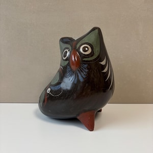 Könnte beinhalten: Handgefertigte Eulenfigur aus Keramik. Die Eule ist überwiegend dunkelbraun mit grünen und weißen Akzenten an Kopf und Flügeln. Sie hat einen roten Schnabel und rote Füße und ist mit blauen und weißen floralen Details bemalt.