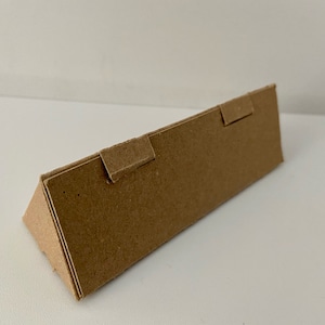 Puede incluir: Una caja de cartón marrón con dos solapas dobladas hacia abajo. La caja está doblada en forma de triángulo.