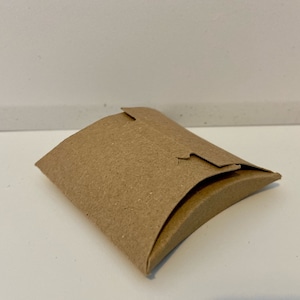 Op de afbeelding: Een bruine kartonnen kussenbox met een gevouwen klep.